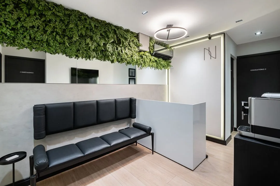 Sala de espera da clínica, com banco estofado preto, balcão claro e jardim vertical suspenso